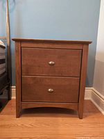 front view of nightstand showing two drawers, brushed nickel pulls, medium-brown finish