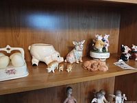 Shelf view showing egg cruet, pig planter, pastel pig, piglets, terracotta pig, music box, dancing pig figurine