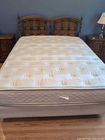 Queen mattress on box spring with wooden headboard and nightstands partially visible
