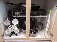 Cabinet view showing cookware, mugs on tree, kettle, lids, grater, cutting board