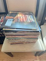 Stack of vinyl LPs on chair, top record Kenny Rogers "Kenny" with auction tag