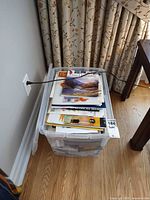 Overview of plastic bin filled with art books, pads and papers