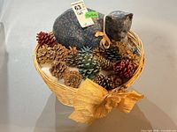 Top view of wicker basket with stuffed cat, pinecones, dried florals and bow