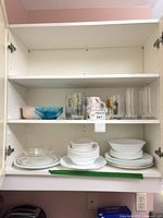 Cabinet shelves showing stacks of white Corelle plates and bowls alongside glassware