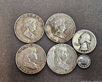 Obverse of four Franklin half dollars, one Washington quarter, one 1 g silver round