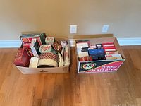 two boxes filled with assorted Christmas tins, plates and boxed lights