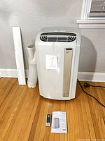 Front view of portable air conditioner with hose, window panel, remote and manual