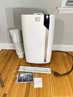 Front view of portable air conditioner with exhaust hose, window panel, remote, manual and power cord