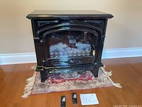 Front view of gloss black electric fireplace stove with remotes on rug