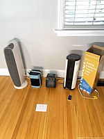 All four devices lined up: tower fan, blue evaporative fan, small black heater, Senville heater with box