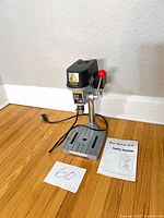 Full view of drill press on floor with manual visible