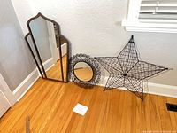 Arched mirror, round scroll mirror and wire star on floor against wall