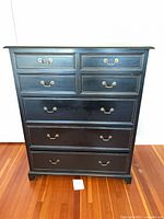 Front view of black painted tall dresser showing five drawers and brass-tone pulls