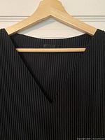 Close-up of V-neck and COS label on pleated fabric