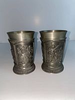 Two metal cups side by side with relief scenes