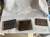 Three tablets lined up showing screens and charger