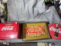 Three Coca-Cola items: red cooler-style radio, framed sign, round metal sign