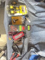 All five items laid out on cloth: charger box, tie-downs, strap wrench, digital gauge, alternator tester