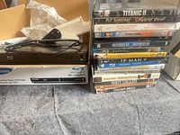 Blu-ray player on carton, remote, power lead, stack of movie discs