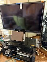 Sharp AQUOS TV on black glass stand with other electronics visible