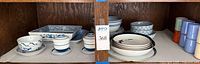 Cabinet shelf with assorted blue and white dishware and white bowls with black rims