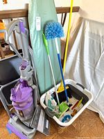 Group view of vacuum, ladder, ironing board, cleaning tools in bin