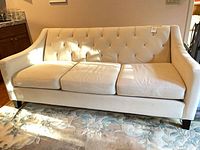 Full front view of ivory three-seat sofa showing cushions, tufted back, and sloped arms.