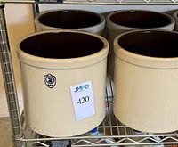 Four matching stoneware crocks on shelf, cream exterior, brown interior