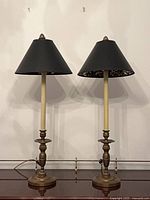 Both brass candlestick lamps side by side with black shades visible