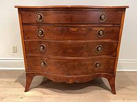 Full front view showing serpentine curve, four drawers, brass pulls, shaped apron, tapered legs