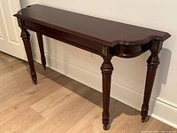 Front angled view of wood console table showing brass accents and turned legs