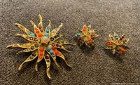 Front view of brooch and earrings showing multicoloured stones and faux pearl