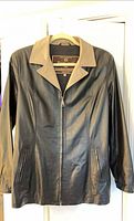 Front view of black leather jacket with beige collar and zip pockets