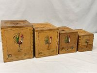 Front view of four graduated wooden canisters with rooster motif