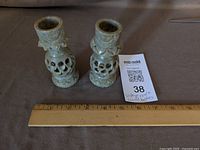 Pair of carved green stone candle holders on cloth with ruler for scale