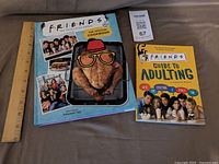 Both books with ruler for scale: Friends: The Official Cookbook and Friends Guide to Adulting
