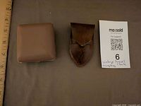 Closed brown case of folded travel clock, leather pouch beside ruler