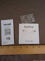 Overall lot showing earrings on Boma card and two ear cuffs in bag with ruler for scale