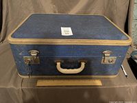 Front view closed blue suitcase, cream trim, chrome latches, initials A.E., key in lock, ruler for scale