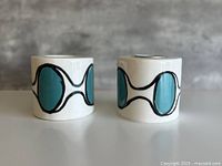 Front view of both cylindrical ceramic candle holders showing teal oval design