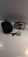 Front view of Canon Sure Shot Owl camera with case and cord visible