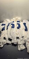 Pile of five white hockey jerseys showing blue numbers on four