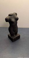 Front view of black pottery torso statue on base