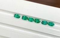 Six oval emeralds lined on white ridged surface