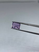 Emerald-cut amethyst held by tweezers, side view
