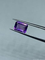 Amethyst held by tweezers showing emerald cut and color
