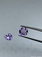 Two faceted round light purple amethysts, one held by tweezers