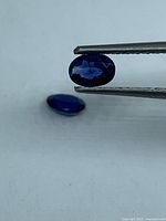 Oval blue sapphire held by tweezers with second stone on surface