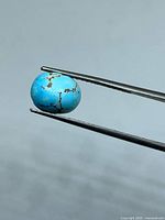 Front view of turquoise oval cabochon held by tweezers