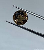 Loose round tourmaline held by tweezers showing color and cut